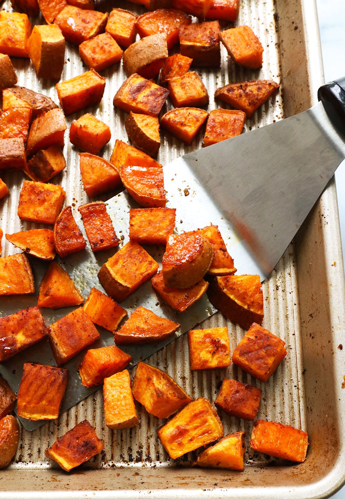 roasted sweet potatoes with a metal spatula on a pan.