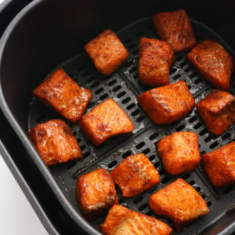 salmon bites cooked in a black air fryer basket.