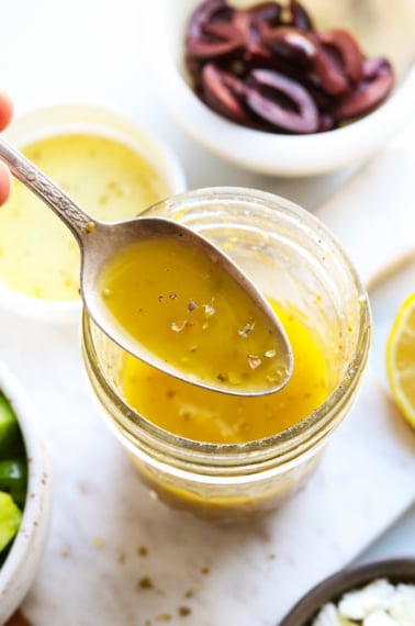 Greek dressing lifted on a spoon from the glass jar.