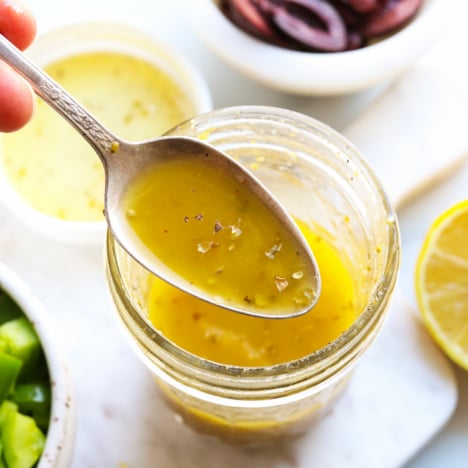 Greek dressing lifted on a spoon from the glass jar.