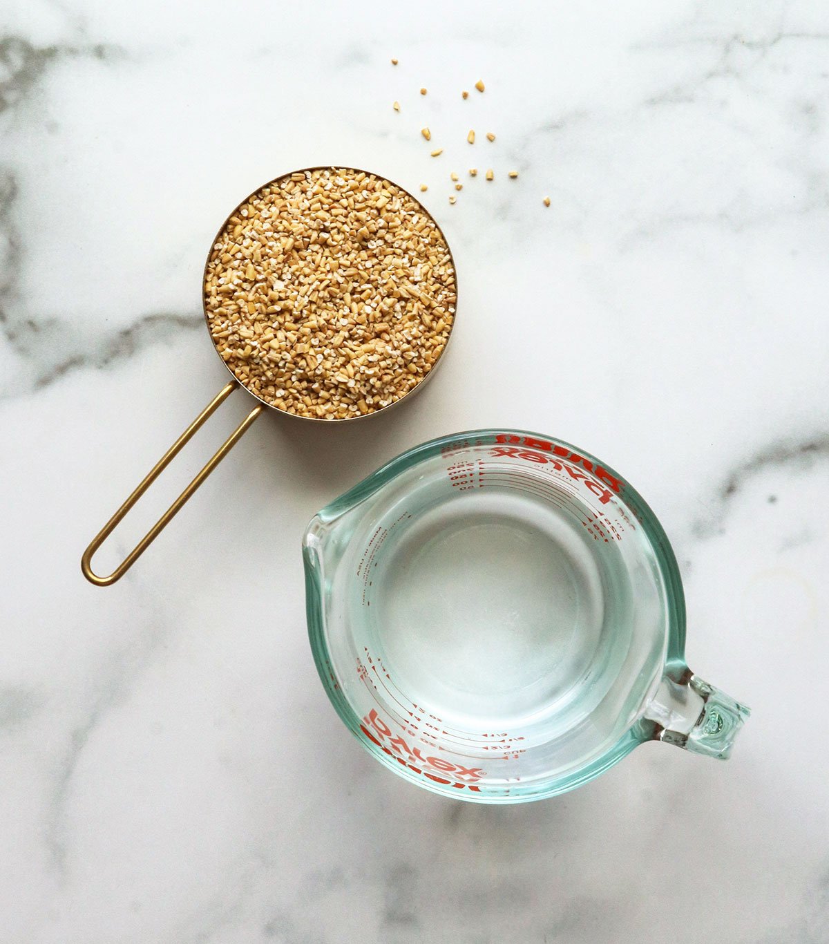 steel cut oats and water in measuring cups on a marble surface.