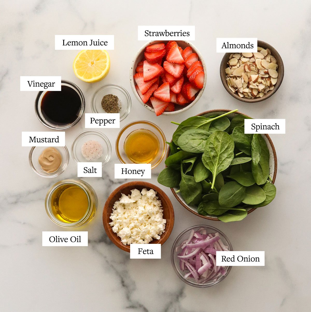 strawberry spinach salad ingredients labeled on marble surface.