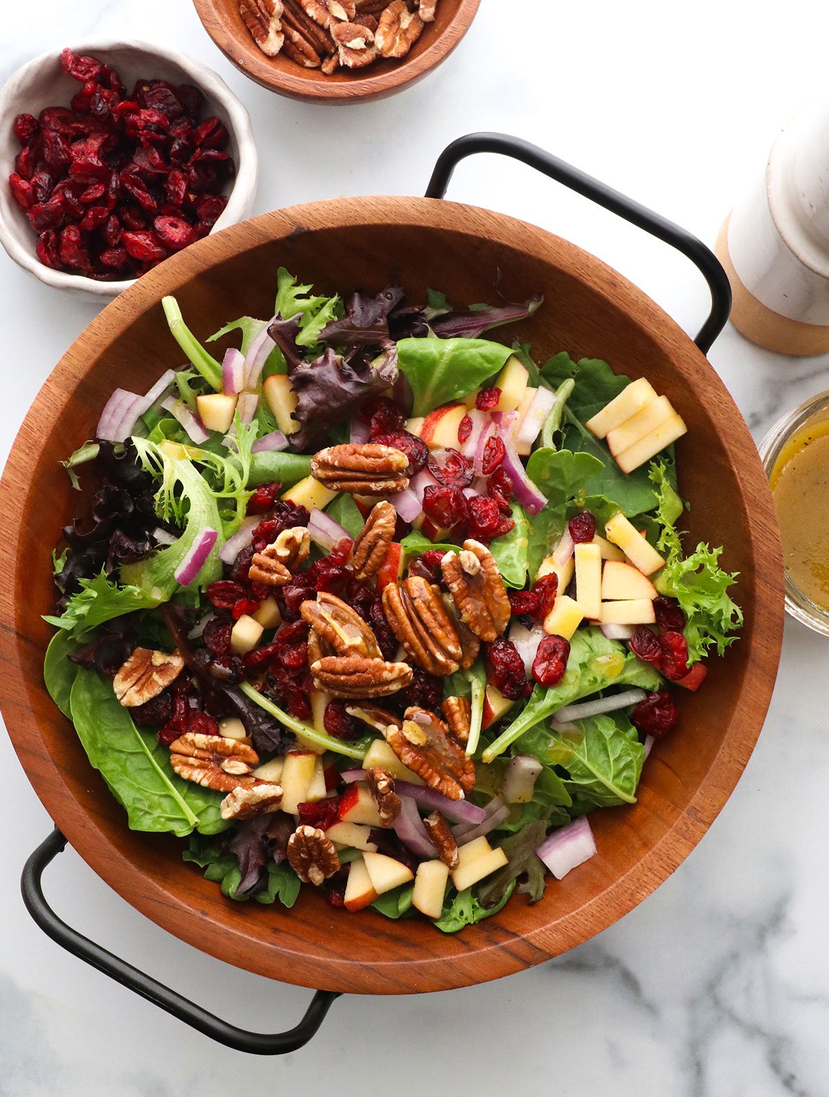 Pecans, apples, dried cranberries, and dressing added to a bowl of greens. 