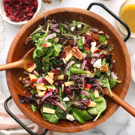 thanksgiving salad tossed with two wooden spoons near a bowl of cranberries.