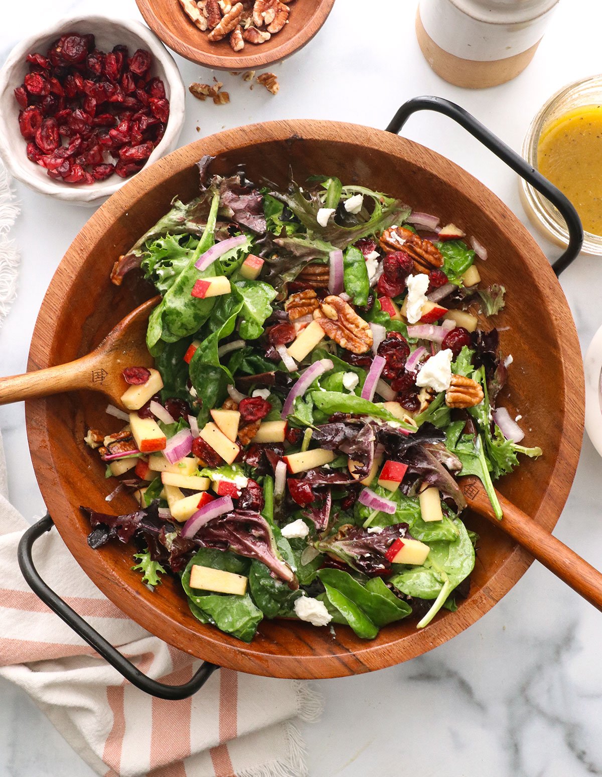 thanksgiving salad tossed with two wooden spoons near a bowl of cranberries.