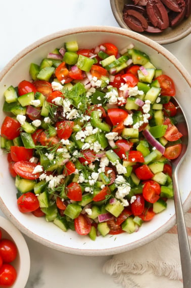 feta and fresh dill sprinkled on a Greek salad in a white bowl.