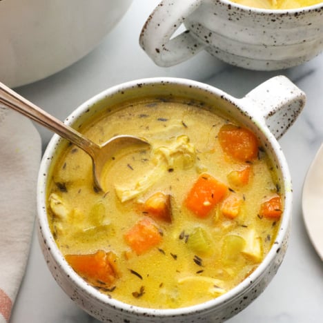 turmeric chicken soup served in white mugs with a spoon.