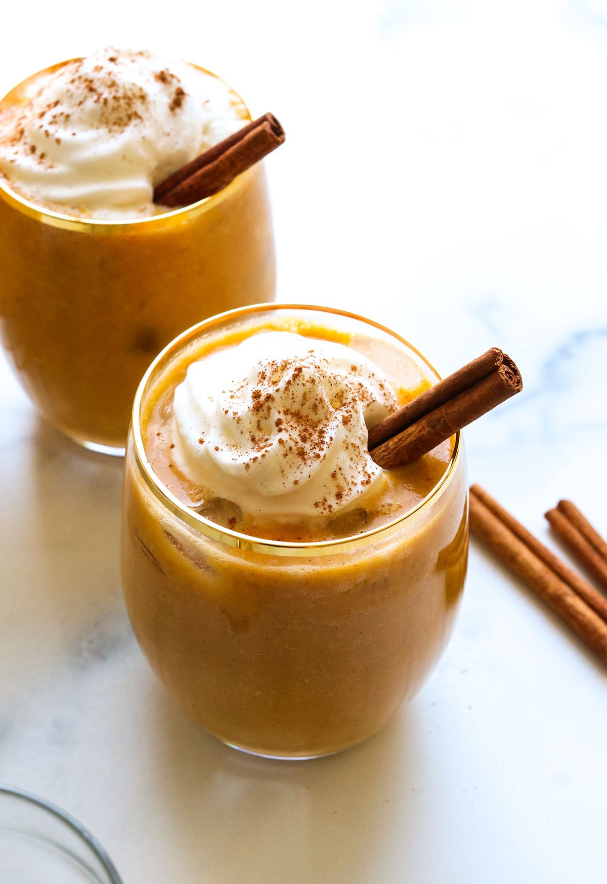 two glasses of vegan eggnog topped with coconut whip and cinnamon sticks.