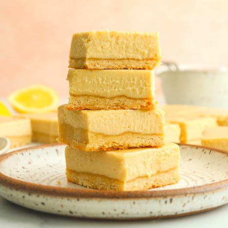 vegan lemon bars stacked in front of pink background.