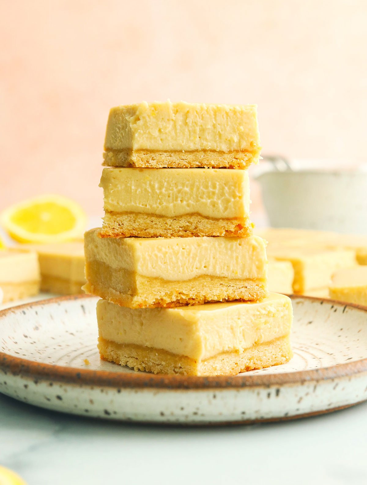 vegan lemon bars stacked on a white plate with pink background.