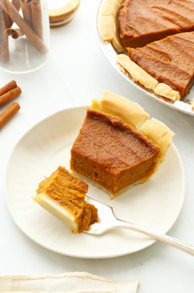 Vegan Pumpkin pie slice cut with a fork on a white plate.