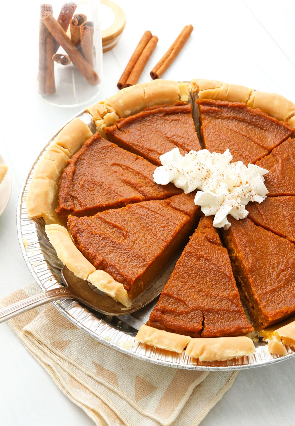 vegan pumpkin pie topped with coconut whipped cream and sliced.