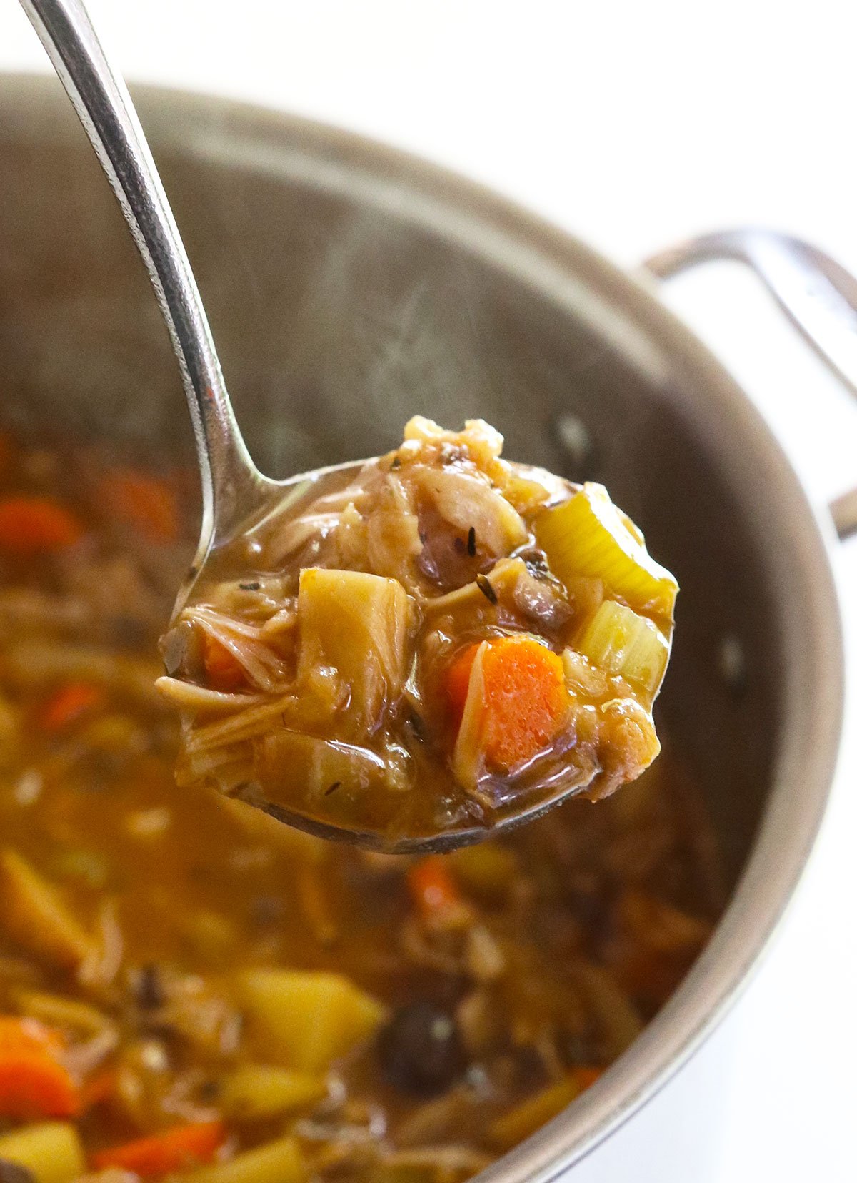 vegetarian stew lifted on a ladle from a soup pot.