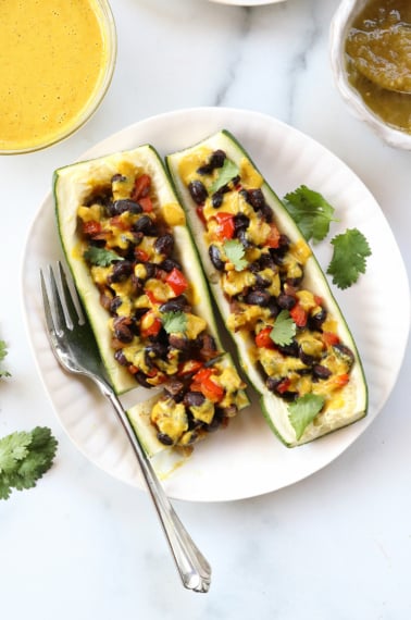 vegan stuffed zucchini boats on a white plate with a fork.