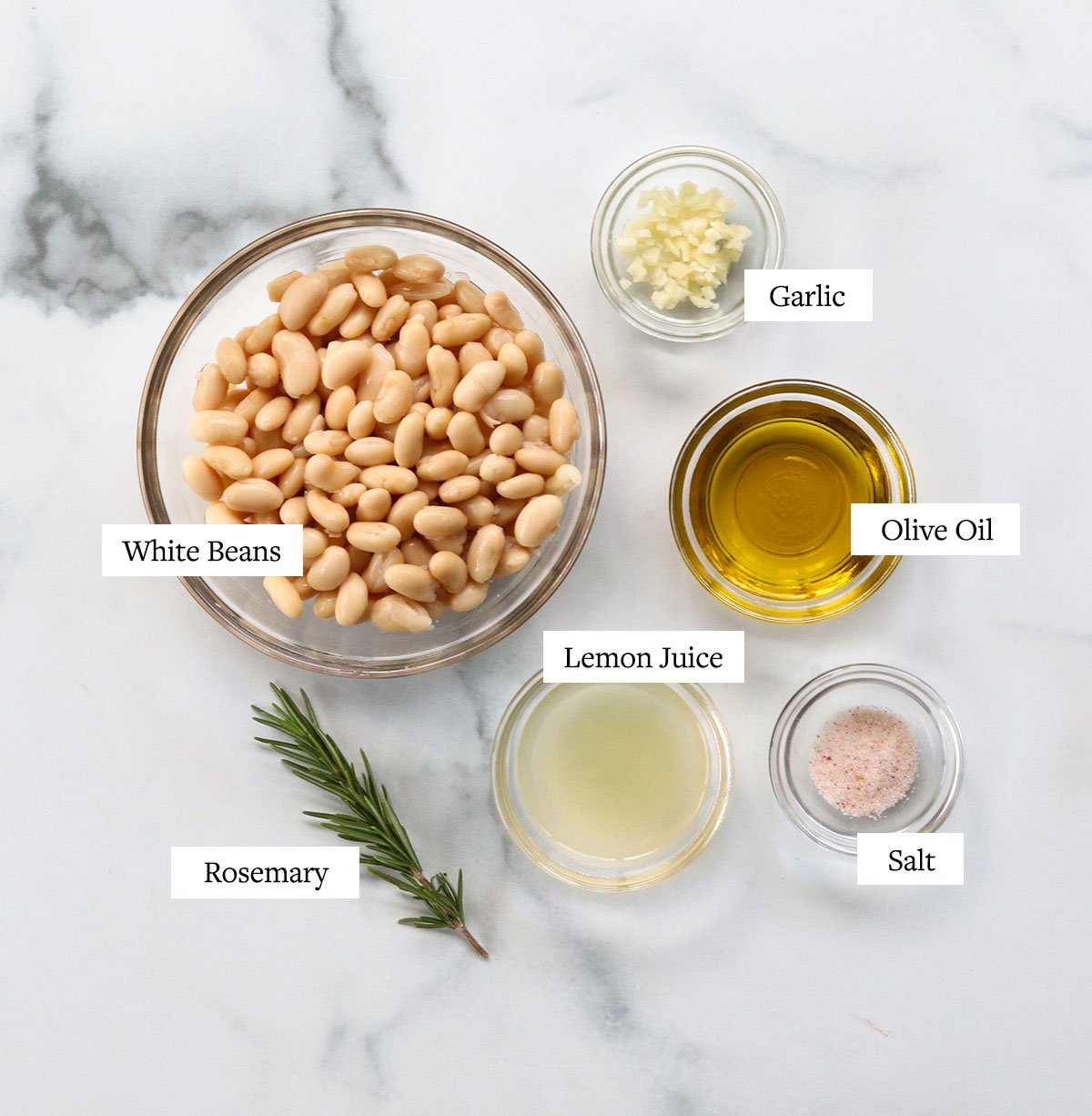 white bean dip ingredients labeled in glass bowls on white surface.