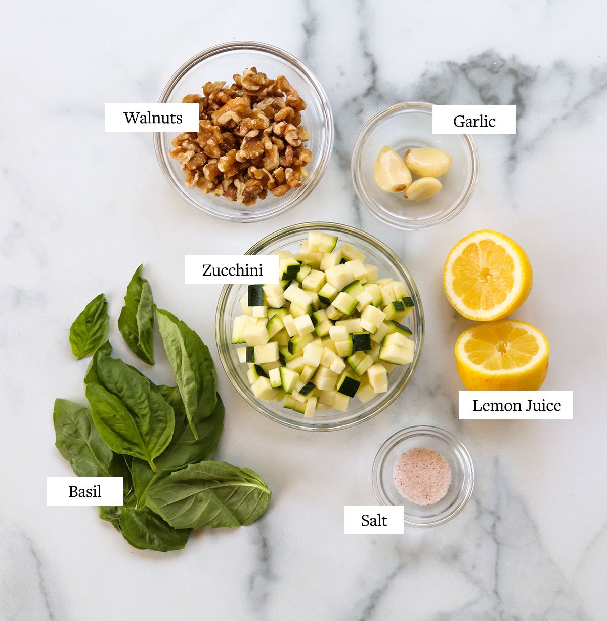 zucchini pesto ingredients labeled on a marble surface.